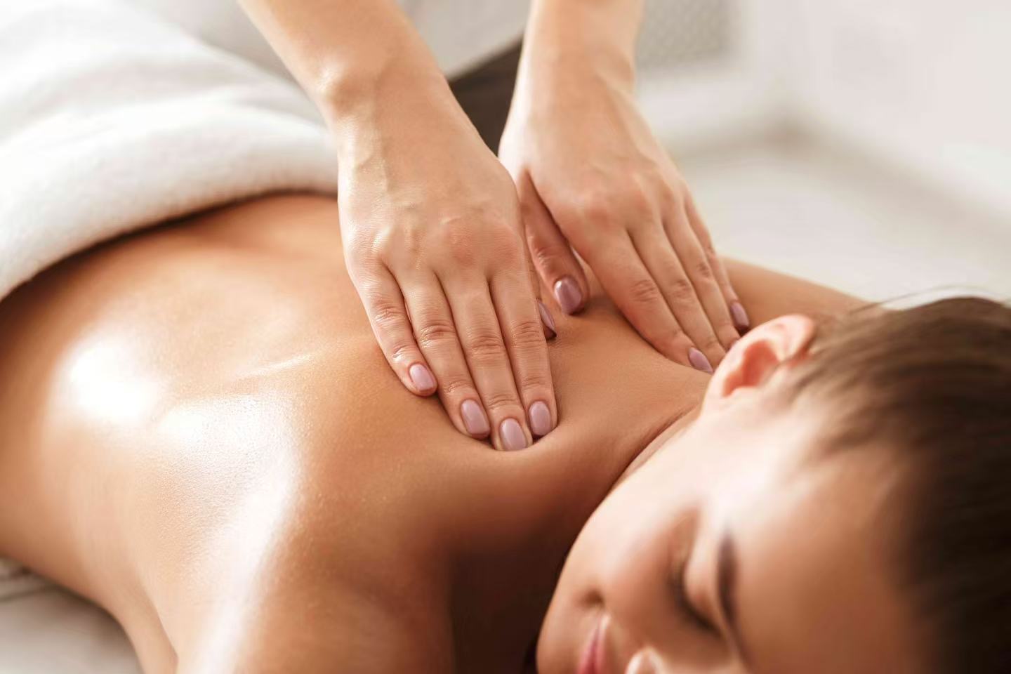 Therapist's hands massaging a relaxed guest's upper back and shoulder